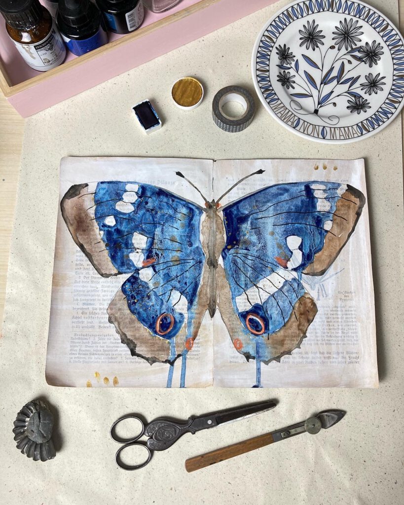 Ein gemalter Schmetterling im Art Journal als Stillleben mit Schere und Feder fotografiert